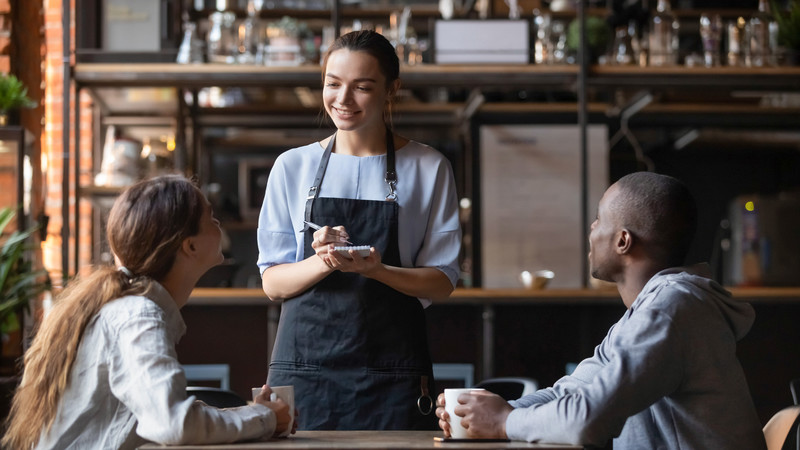 Servitris som tar beställning av ett sällskap som sitter till bords inne på restaurang.
