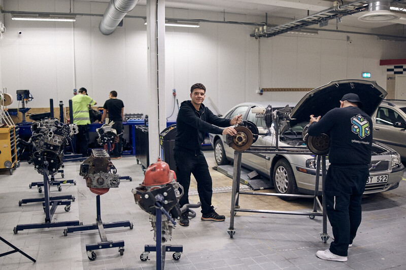 Garage med bilar och delar till bilar där skolelever reparerar motorhuv.