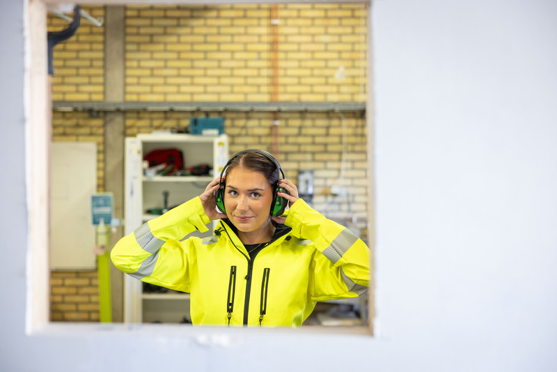 Kvinnlig skolelev som tittar in i kameran och håller händerna på sina hörselkåpor.