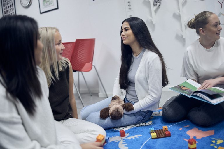 Kvinnliga elever sitter i ring och läser i en bok för varandra.