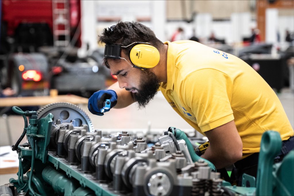 Elev undersöker en motor med ficklampa i verkstadsmiljö.