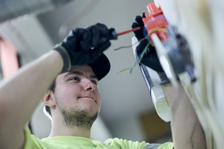 Manlig elev som står och skruvar på en sladd som går till el i väggen.