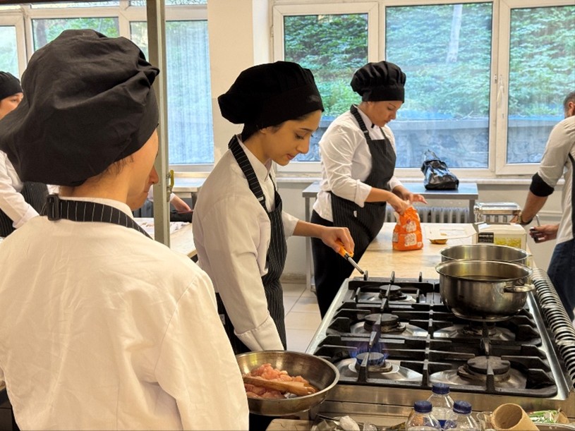 Personer i kockkläder lagar mat vid en spis i ett kök