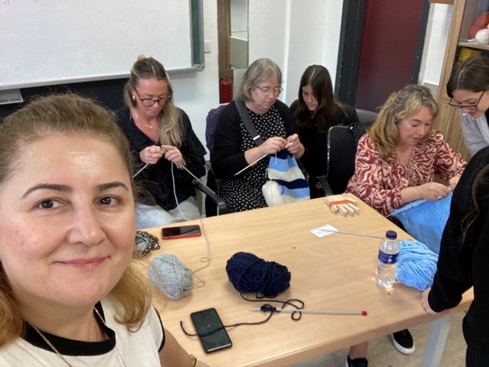 Grupp som sitter runt ett bord och stickar, med en person som tar en selfie.