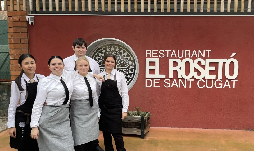 Fem elever från Yrkesgymnasiet Göteborg, klädda i serveringskläder med vita skjortor, förkläden och slipsar, står tillsammans utanför restaurangen El Rosetó de Sant Cugat.