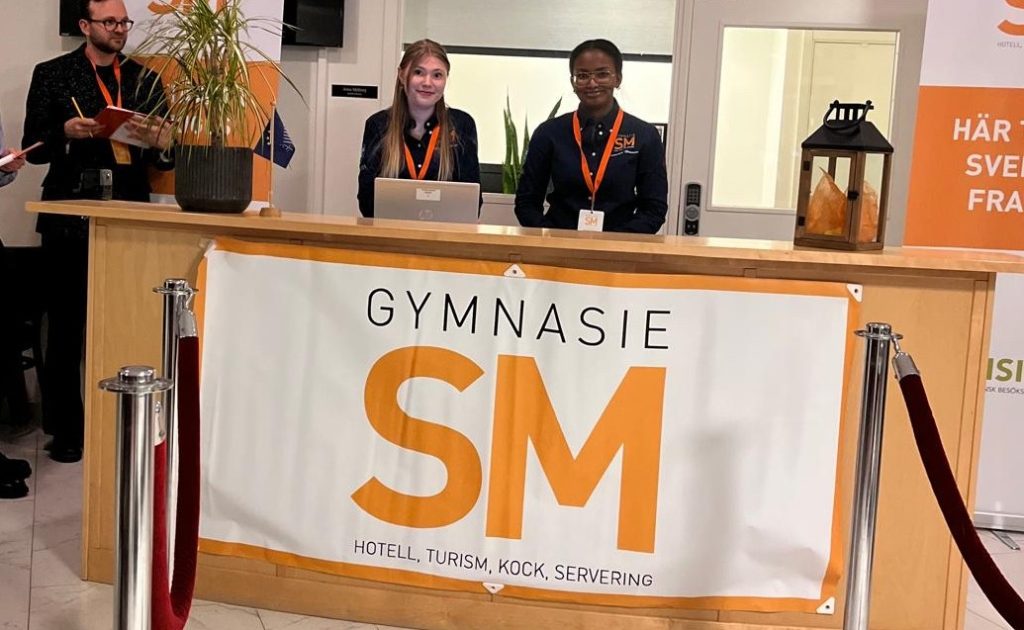 Två elever från Yrkesgymnasiet Umeå står bakom receptionsdisk på Gymnasie-SM.
