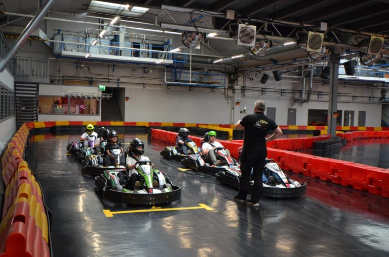Elever sitter i go-kart bilar på bana inomhus.